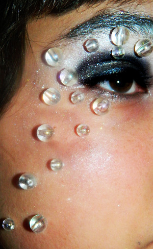 Using a matte white, cover your whole eyelid, then taking a black cover eyelid and crease, line your eyes with cream midnight blue eyeliner....then using liquid latex or eyelash glue, glue rainbow reflective clear beads to your face in any design you want...DONE!!