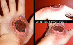 This was my first attempt at a major area wound, and I think it didn't come out so bad. Anyways I prepped my hand by shaving it, ALWAYS shave the area your going to apply latex it will cling to your hair and will pull it out when your removing it. I then applied about 7 good layers of latex with a disposable triangle blending sponge; I used a blow dryer on each layer to speed up the process and once each layer was dry I powdered it with a shade that matched my skin tone ( I used Manic Panic's Vampires Veil in Moonlight) so the latex blended in with my skin tone. After that I agitated the center of the latex and tore a hole in it. I then took some cotton balls and began to stretch and rip them to make them look like eaten up flesh. I then applies a thin layer of latex on the area of the wound that was open and put the ripped cotton on the latex. Next I took my stage blood and soaked it into the cotton. Around the edges of the wound I applied a matte black shadow to add depth to the wound. I then took various shades of lipsticks ( mostly red's and eggplant shades) and blotted them sporadically on and around the untorn latex and blended it out. I then used some matte dull blue and yellow eye shadows on the same area to create a bruising effect. I then finished it off with some stage blood blotted around the wound