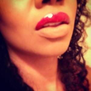 Red cream lipstick on upper lip topped with red shimmer gloss; lower lip blotted with foundation and powder.