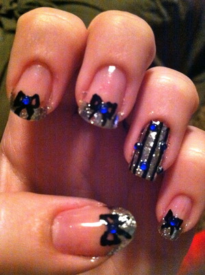 Silver foil french tips with black bows and a blue rhinestone in the middle. Accent nail is silver foil with black stripes and blue rhinestones scattered across the nail.
