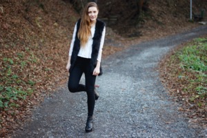Black faux fur gilet. Features sleeveless styling and open-front. 