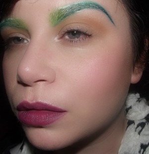 Bold green ombre eyebrows paired with a matte purple lip, cool pink complexion and neutral eyes. 
