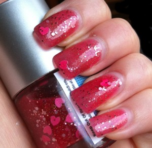 A pink jelly polish with gold holographic glitter, pink glitter, pink hearts, and white hex.