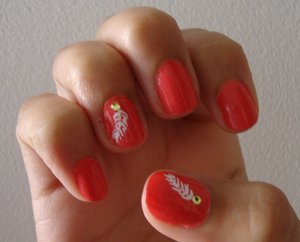 Coral nails, with a white feather painted on ring finger and thumb, along with a peridot-colored nail gem.