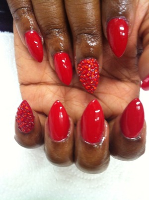 Red stones on red nail lacquer .  Stiletto shaped acrylic nails. 